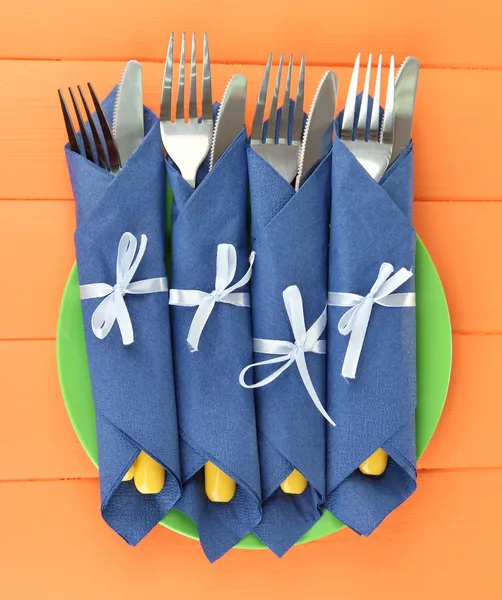 Forks and knives wrapped in blue paper napkins, on color wooden background — Stock Photo, Image