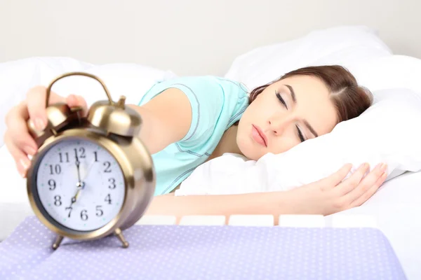 Beautiful young woman sleeping on bed with alarm clock in bedroom — Stock Photo, Image