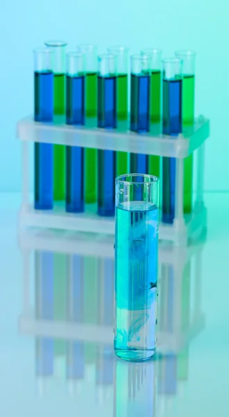 Identical test tubes and hand on blue background — Stock Photo, Image