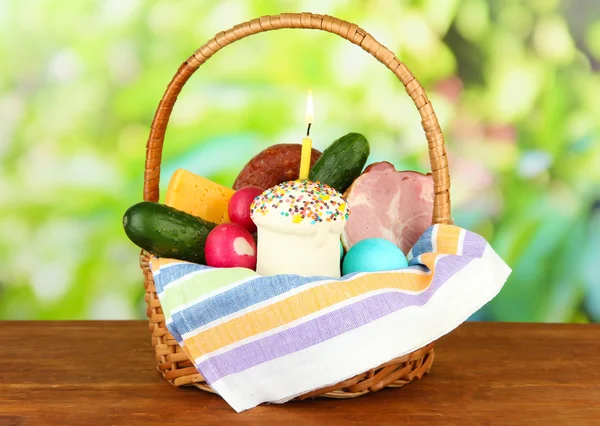 Easter basket: Conceptual photo of traditional easter food in wicker basket, on wooden table on bright background