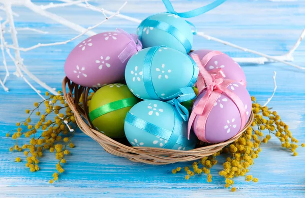 Пасхальные яйца в корзине и цветы мимозы, на синем деревянном фоне — стоковое фото