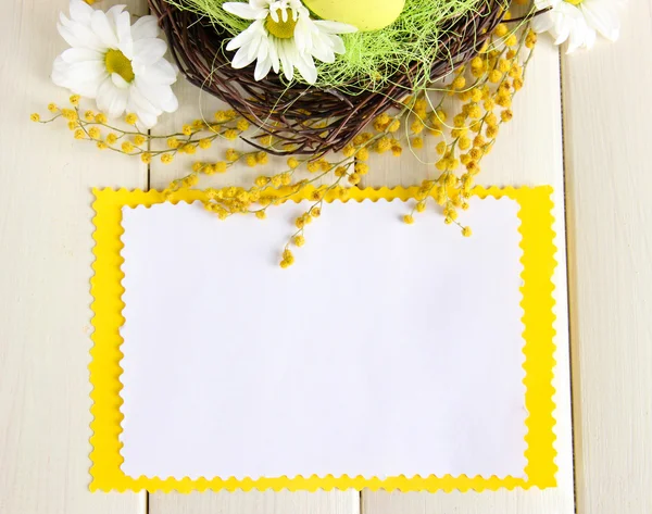 Carta vuota con uova di Pasqua e fiori di mimosa, su fondo di legno bianco — Foto Stock