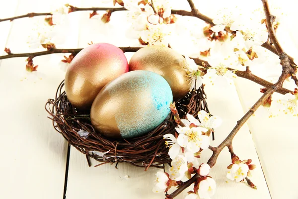 Huevos de Pascua en nido con ramas florecientes sobre mesa de madera — Foto de Stock