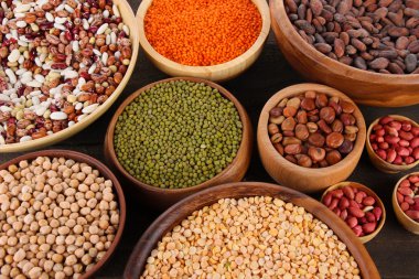 Different kinds of beans in bowls on table close-up clipart