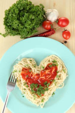 Cooked spaghetti carefully arranged in heart shape and topped with tomato sauce, on wooden background