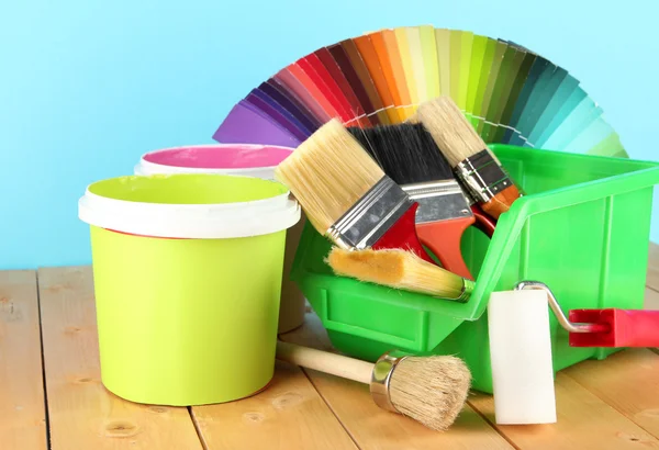 Pots de peinture, pinceaux et échantillons colorés sur table en bois sur fond bleu — Photo