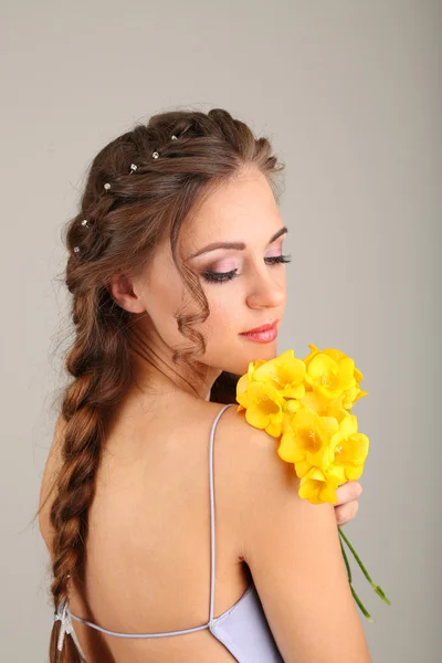 Jeune femme avec une belle coiffure et des fleurs, sur fond gris — Photo