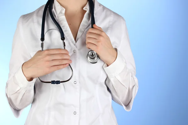 Médecin avec stéthoscope dans les mains sur fond bleu — Photo