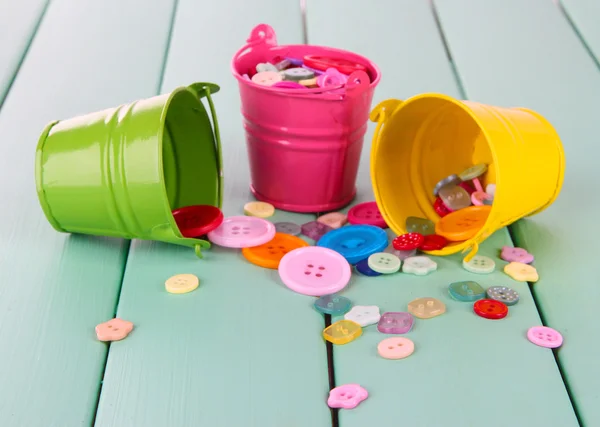 Colorful buttons strewn from buckets on wooden background — Stock Photo, Image