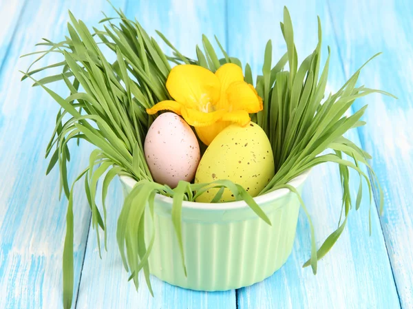 Пасхальные яйца в миске с травой на синем деревянном столе — стоковое фото