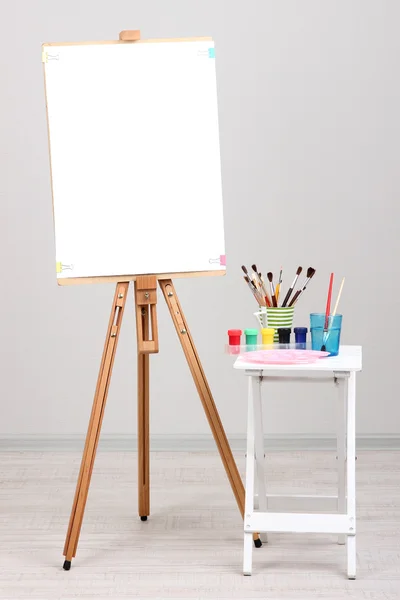 Wooden easel with clean paper and art supplies in room — Stock Photo, Image