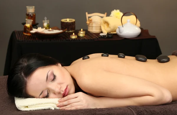 Hermosa joven en el salón de spa con piedras de spa, sobre fondo oscuro — Foto de Stock