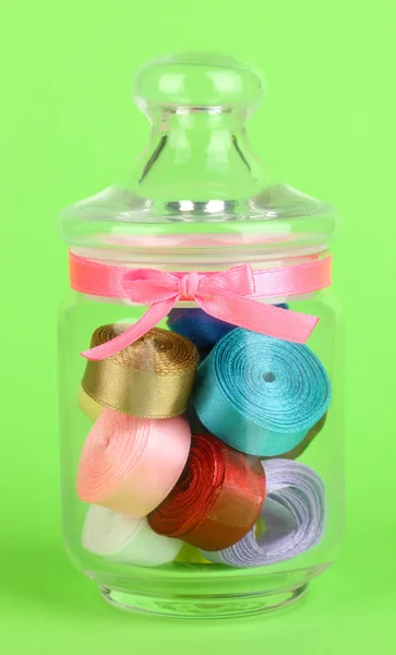 Pot en verre contenant divers rubans de couleur sur fond vert — Photo