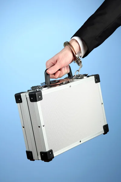 Hand with handcuff and suitcase, on color background — Stock Photo, Image