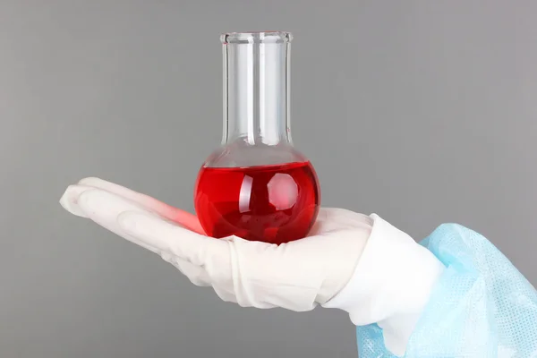 Tubo de vidrio con fluido en la mano del científico durante la prueba médica sobre fondo gris —  Fotos de Stock