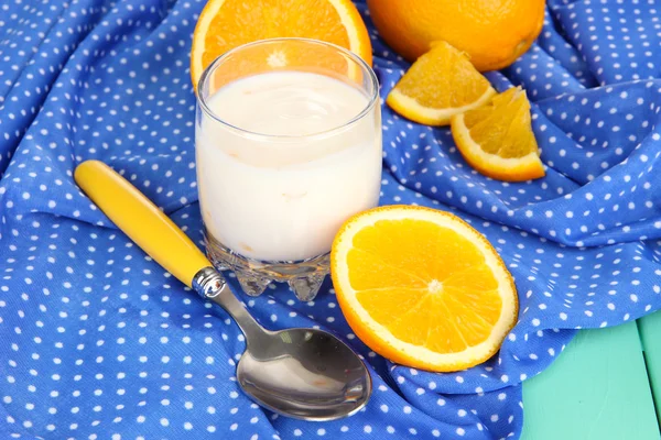 Delicioso yogur en vaso con naranja sobre mantel azul —  Fotos de Stock