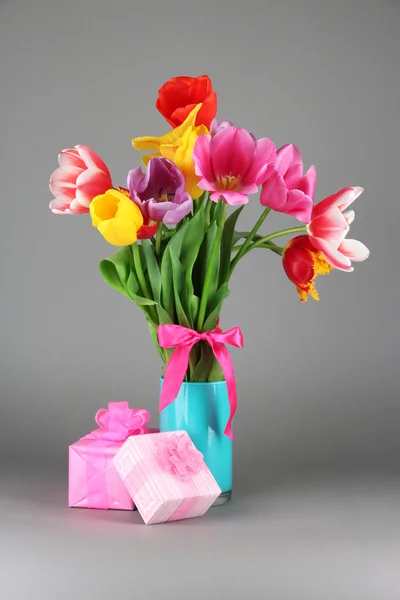 Schöne Tulpen im Strauß mit Geschenken auf grauem Hintergrund — Stockfoto