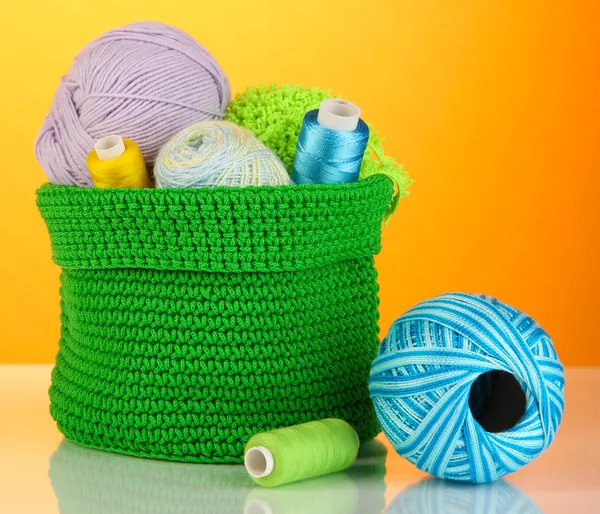 Kolorowe przędzy na drutach w zielony koszyk na pomarańczowym tle — Zdjęcie stockowe