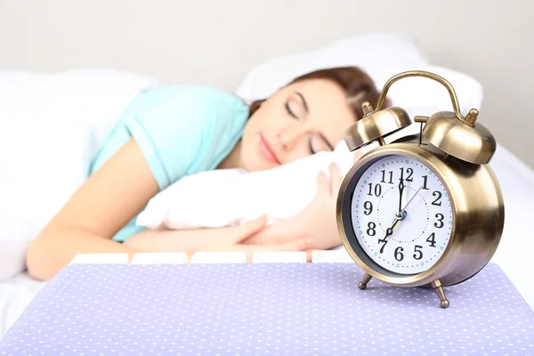 Beautiful young woman sleeping on bed with alarm clock in bedroom — Stock Photo, Image