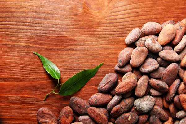 Cocoa beans with leaves on wooden background — Stock Photo, Image
