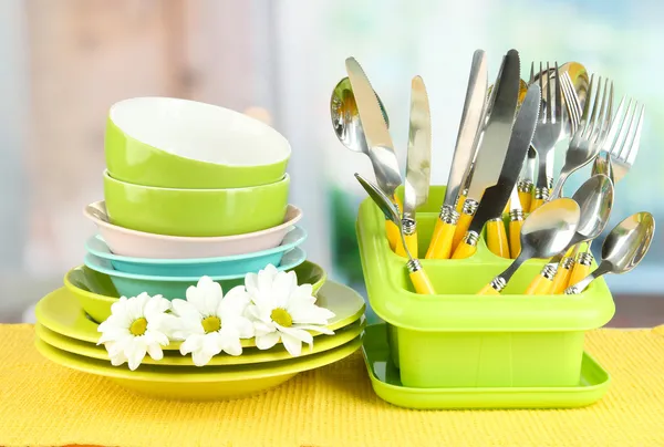 Placas, tenedores, cuchillos, cucharas y otros utensilios de cocina en servilleta de color, sobre fondo brillante —  Fotos de Stock