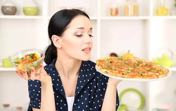 Mooi meisje selecteert pizza of dieet op keuken achtergrond — Stockfoto