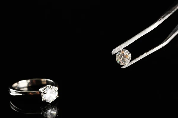 Crystal (diamant) in het pincet en ring, schijnt op zwarte achtergrond — Stockfoto