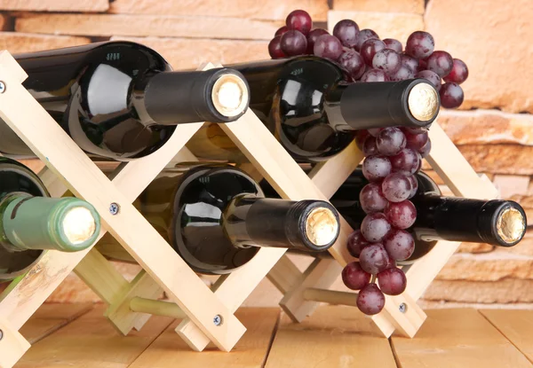 Botellas de vino colocadas sobre soporte de madera sobre fondo de pared de piedra —  Fotos de Stock