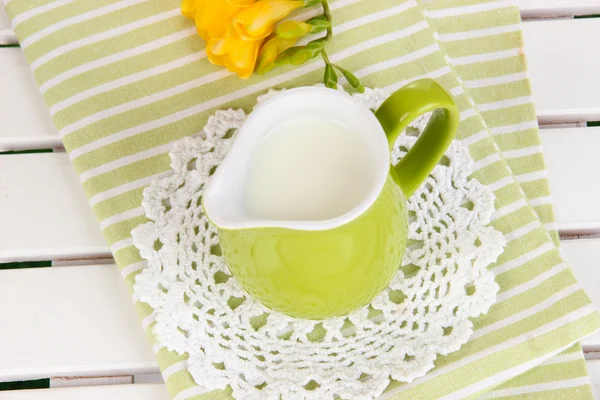 Green jug with milk on napkin on wooden picnic table close-up — Stock Photo, Image