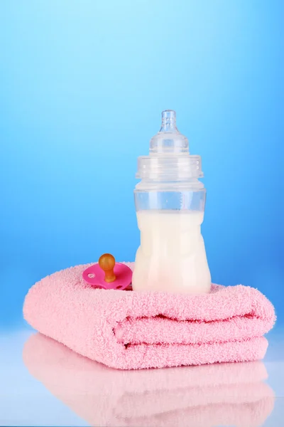 Fles voor melk met handdoeken en tepel op blauwe achtergrond — Stockfoto
