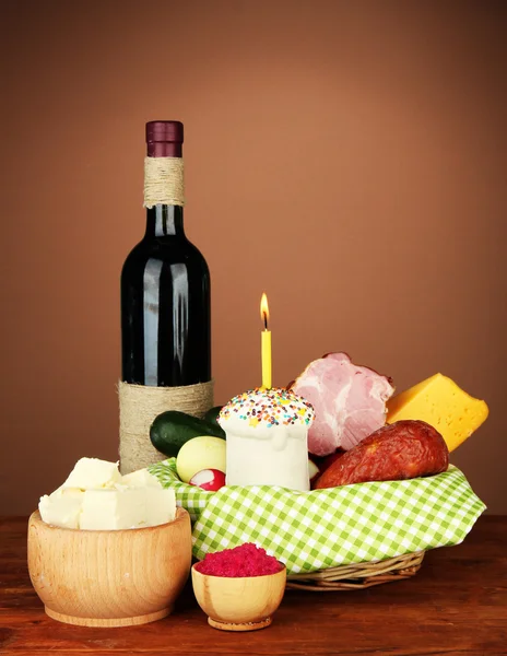 Пасхальная корзина: Концептуальное фото традиционной пасхальной еды в плетеной корзине, на деревянном столе на цветном фоне Стоковое Фото