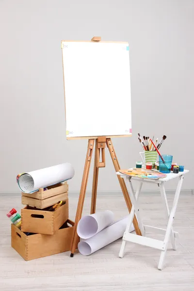 Wooden easel with clean paper and art supplies in room — Stock Photo, Image