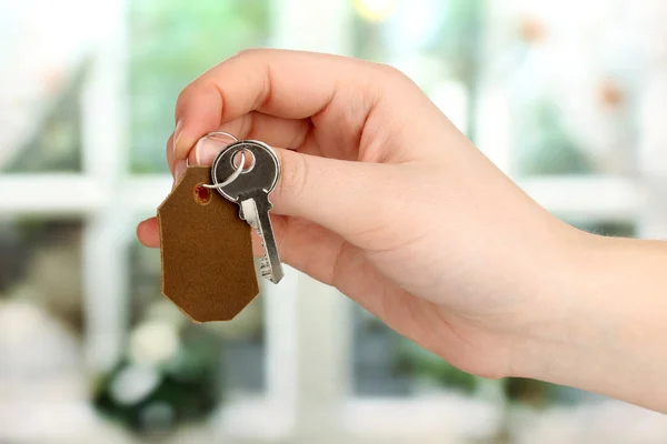 Nyckel med läder prydnadssak i handen på fönsterbakgrund — Stockfoto