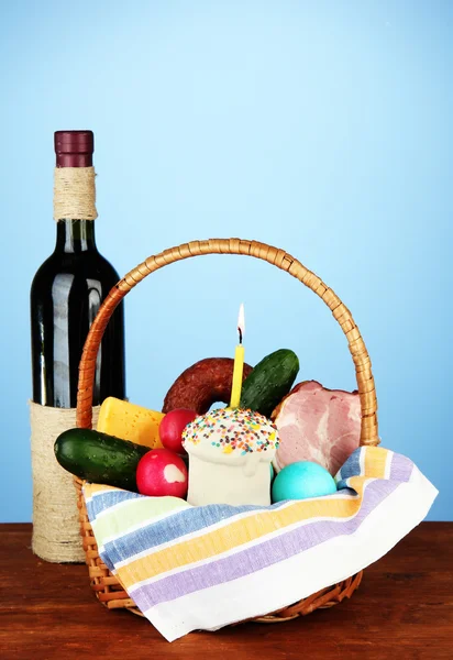 Easter basket: Conceptual photo of traditional easter food in wicker basket, on wooden table on color background