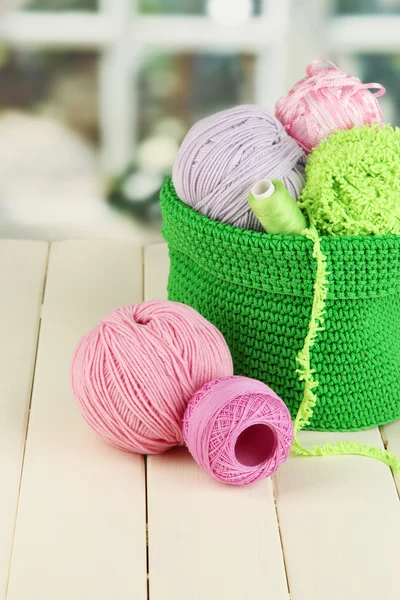 Colorful yarn for knitting in green basket on wooden table on window background — Stock Photo, Image