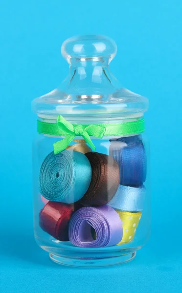 青色の背景にさまざまな色のリボンを含むガラスの瓶 — ストック写真
