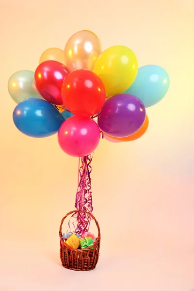 Many bright balloons and basket with gifts on orange background — Stock Photo, Image