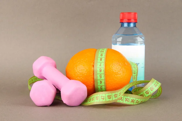 Laranja com fita métrica, halteres e garrafa de água, sobre fundo colorido — Fotografia de Stock