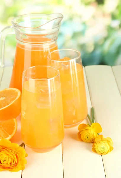 Очки и кувшин апельсинового сока на деревянном столе, на зеленом фоне — стоковое фото