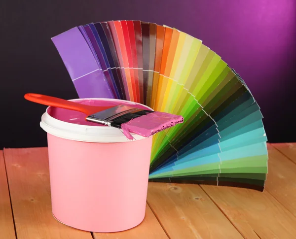Горшок с краской, кисть и цветные образцы на деревянном столе на темно-фиолетовом фоне — стоковое фото