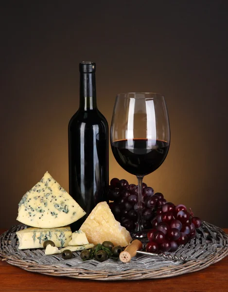 Natura morta raffinata di vino, formaggio e uva su vassoio di vimini su tavolo di legno su sfondo marrone — Foto Stock