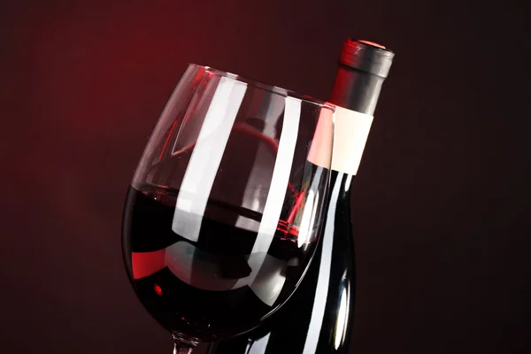 Víno ve sklenici a víno láhev close-up na tmavém pozadí — Stock fotografie