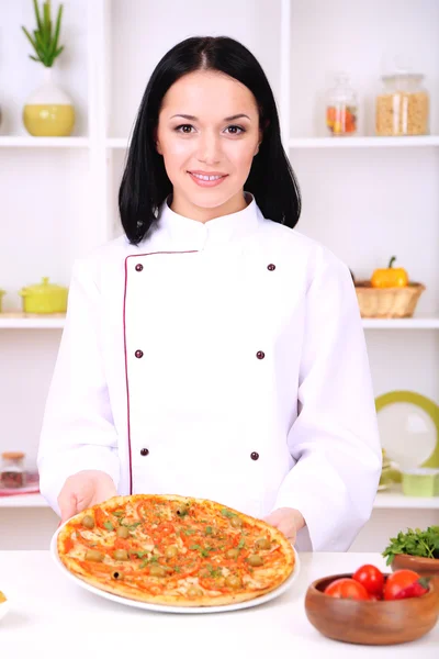 Mooi meisje chef-fornuis met pizza op keuken achtergrond — Stockfoto