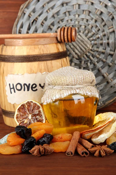 Jar of honey, wooden barrel, drizzler and dried fruits on wooden background — Stock Photo, Image