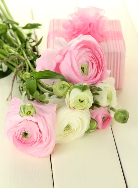 Ranunculus (persian buttercups) and gift, on white wooden background — Stock Photo, Image