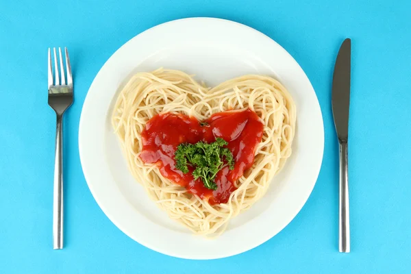 Gekookte spaghetti zorgvuldig gerangschikt in hart vorm en gegarneerd met tomatensaus, op een achtergrond met kleur — Stockfoto