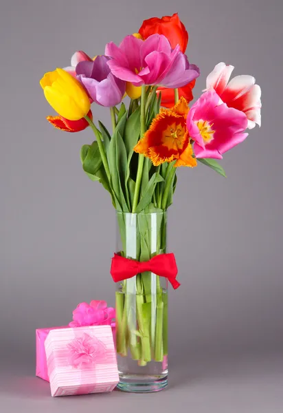 Beautiful tulips in bouquet with gifts on gray background — Stock Photo, Image