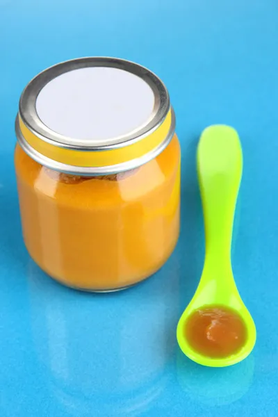 Color spoon for baby food with baby nutrition on blue background — Stock Photo, Image