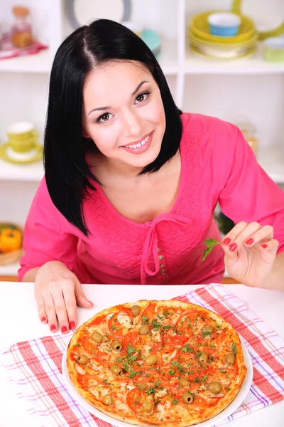 Mooi meisje met heerlijke pizza op keuken achtergrond — Stockfoto