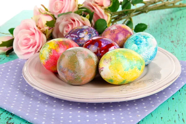 Huevos de Pascua en plato con servilleta y flores en mesa de madera — Foto de Stock